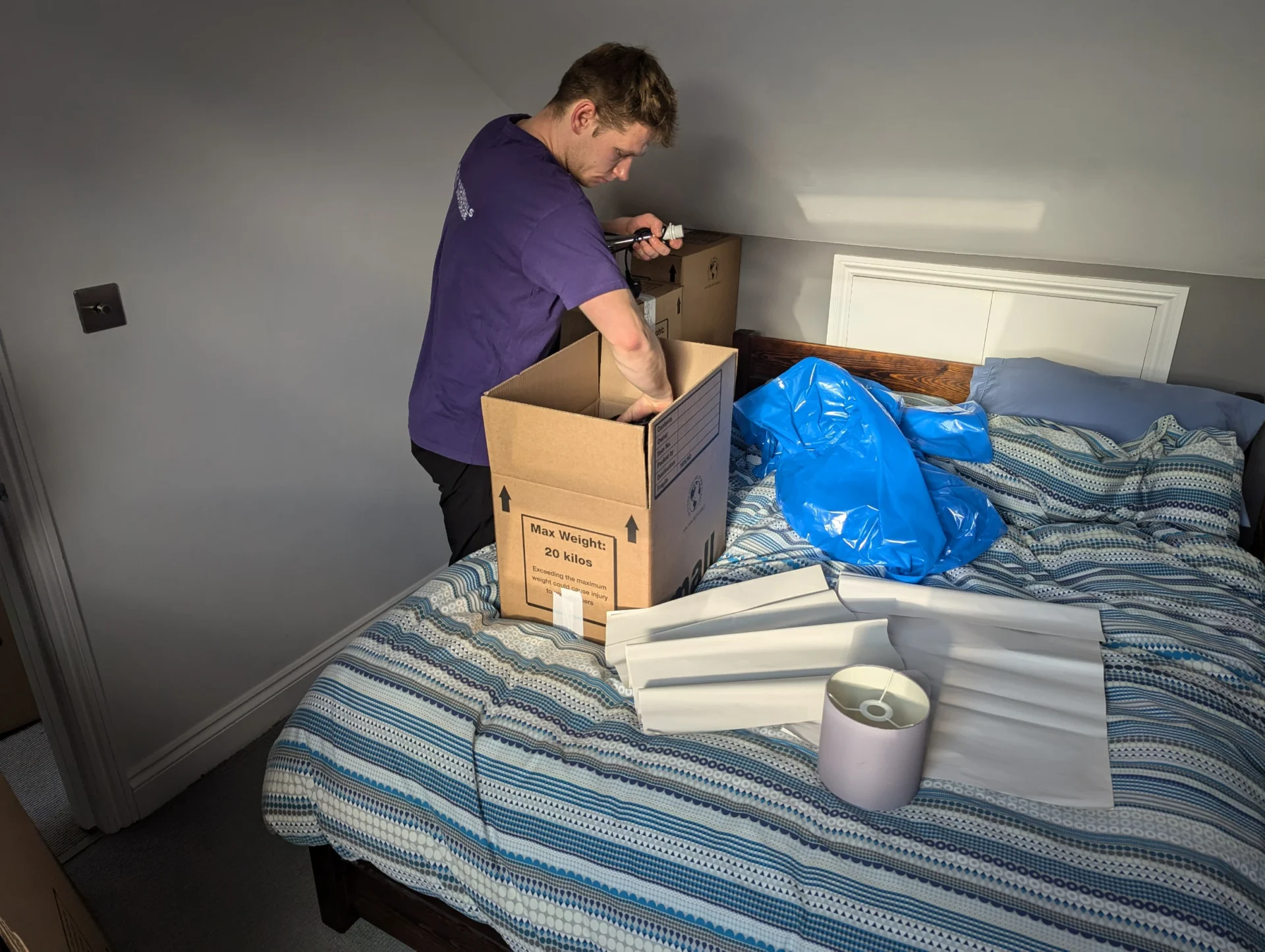 Rad Removals team member packing a lamp, clothes, and bedroom essentials into a cardboard box during a home move in South West London